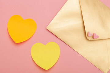 Obraz na płótnie Canvas Golden paper envelope with two hearts from marshmallow and two yellow paper hearts isolated on pink background