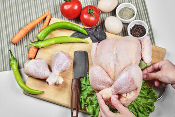 Holding raw whole chicken on wooden board with fresh vegetables and spices