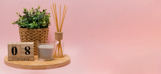 calendar. 8 february composition from a wooden calendar, a flower in a wicker pot, a gray candle in a glass candlestick and an aroma diffuser on a light pink background banner business