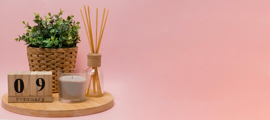 calendar. 9 february composition from a wooden calendar, a flower in a wicker pot, a gray candle in a glass candlestick and an aroma diffuser on a light pink background banner business