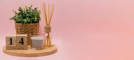 calendar. 14 february composition from a wooden calendar, a flower in a wicker pot, a gray candle in a glass candlestick and an aroma diffuser on a light pink background banner business
