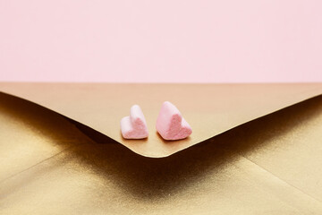 Golden paper envelope with two hearts from marshmallow isolated on pink background