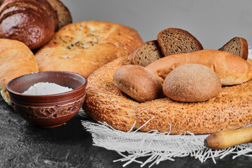 Naklejka premium Various types of bread on dark table with bowl of flour