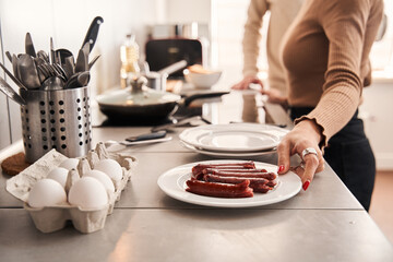 Woman holding plate with sausages while preparing breakfast