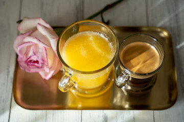 a cup of coffee with glass of orange juice and a rose on a gold tray