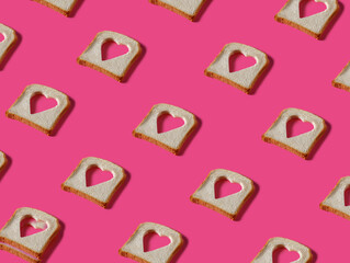 Toasted bread slices with cut in shape of heart on pink background. Minimal Valentines Day, Mother's day, love or romantic food concept. Creative love pattern. Flat lay, top view.