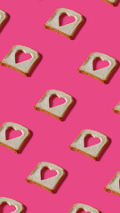 Toasted bread slices with cut in shape of heart on pink background. Minimal Valentines Day, Mother's day, love or romantic food concept. Creative love pattern. Flat lay, top view.