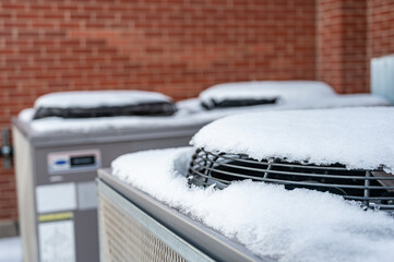 Outdoor mechanical air conditioning units idling during the winter with snow on top of the fans