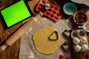 Dough, rolling pin and many heart molds for tablets and cookies with green screen on the table.