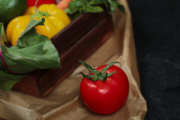 Wooden box of fresh vegetables and juicy tomato on dark background