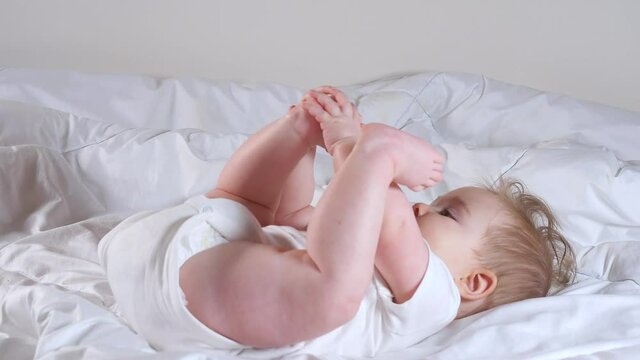 Adorable 7 month baby girl lying on the bed and playing with her legs
