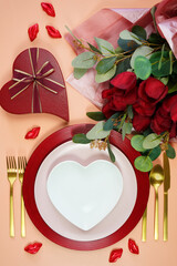 St Valentine's Day dinner table setting with red roses, heart shape gift and lipstick kisses chocolates. Creative top view flatlay layout. Vertical place setting.
