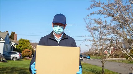 Postal worker hand delivering mail package while walking down a sidewalk wearing a mask