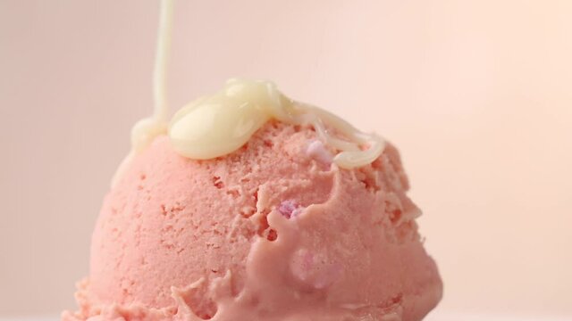 close up of rotating pink ice cream scoop and white chocolate sauce flowing on ice cream