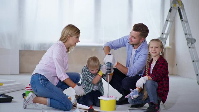 cheerful family with male children with Down Indrome mix pigment to paint walls in apartment during renovation