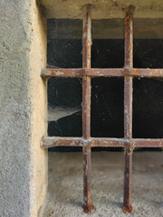 Old and rusted metallic grid  with the spider net in the stone wall