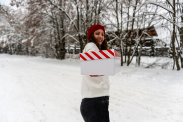 Smiling girl in a red bandage giving a gift on the street in winter