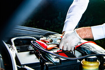 Attaching clips to a car battery under a hood, at night. Jump starting a car.