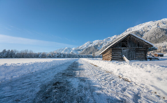 Snow covered walking path through alpine winter landscape with wooden barn in Wildermieming, Tirol, Austria