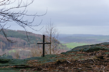 Fototapeta na wymiar small iron cross on rock formation with blurry landscape in background