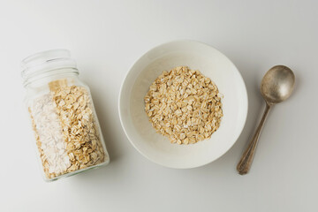 Rolled oats in a bowl and glass jar on white background, top view