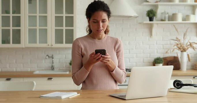 Happy young beautiful woman working on laptop, getting message notification with online lottery win, feeling overjoyed at home, celebrating professional or gambling success, dancing alone in kitchen.