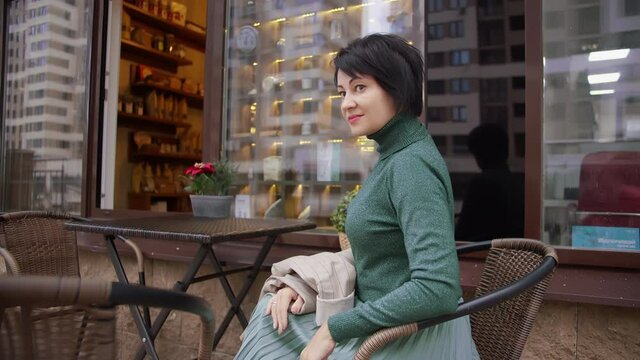 pretty woman in green sits in a cafe on the street looks at the camera and smiles