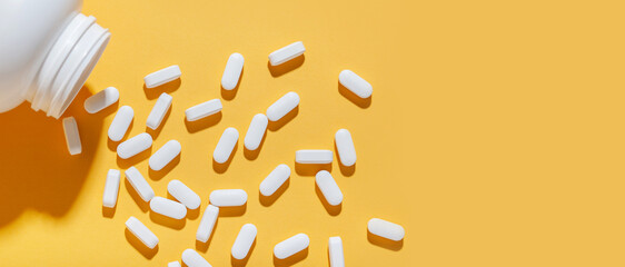 White pills are poured from a jar on a yellow background. Food supplement, multivitamins, medications