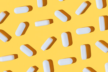 Modern pattern with hard shadows of white pills on yellow background. Food supplement, multivitamins, medications