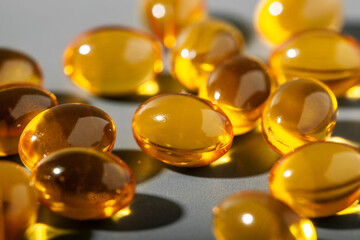 Yellow gelatin capsules on a gray background. Food supplement, vitamin D, omega, vitamin C, multivitamins. Soft focus