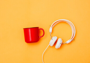 Red cup of coffee and white headphones on yellow background.