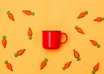 Red cup of coffee and Easter cookie carrots on yellow background
