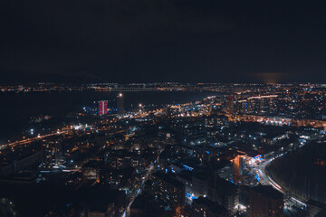 Fototapeta premium Drone view at night, with illuminated streets and dark sky. Beautiful cityscape