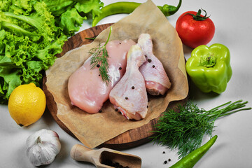 Wooden plate of raw chicken fillet and legs with vegetables on white table