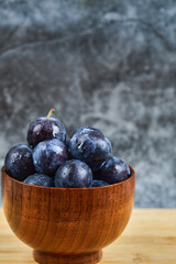 Garden plums in a bowl on wooden table