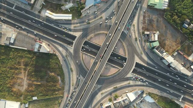 Fast rotated top-down angle aerial drone shot of roundabout and crossing expressway with evening busy traffic.