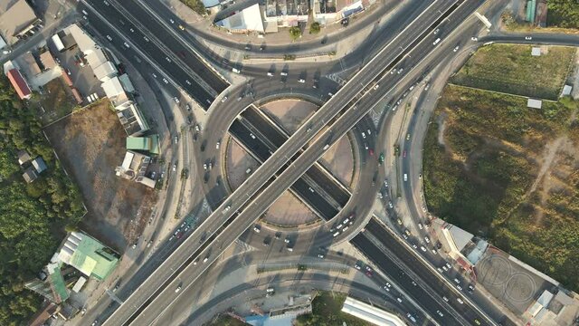 Top-down aerial drone shot of roundabout and x-shaped crossing expressway with evening busy traffic.