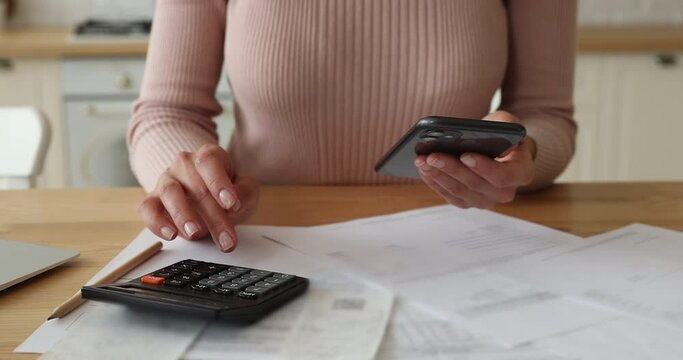 Close up young woman calculating domestic utility bills, making payment online in cellphone e-banking application, managing expenditures or monthly budget, modern technology easy usage concept.