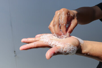 Fototapeta premium Man use soap and washing hands with grey background under the sunlight. Hygiene concept hand detail