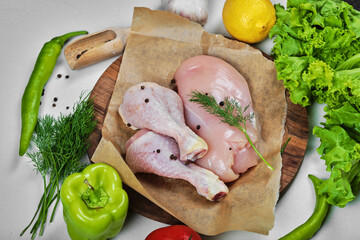 Wooden plate of raw chicken fillet and legs with vegetables on white table