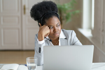 Unmotivated Afro businesswoman in blazer with headphones looking at the window, thinking or...