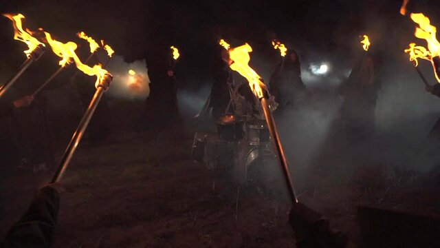 A drummer plays drums in a field at night. Around people with torches.