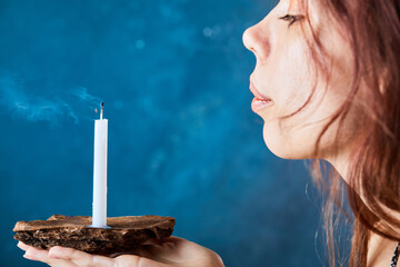 Young woman blowing out candle on blue background