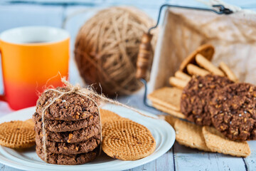 Assorted biscuits in plate and basket and a cup on blue table