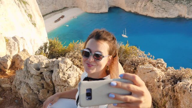 Young woman at Navagio Beach Shipwreck in Zante., taking selfies with smartphone. Lagoon of Zakynthos island, Ionian Sea, Greece