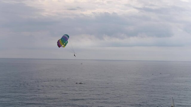A bird's eye view of people parasailing high above a calm ocean on a cloudy day