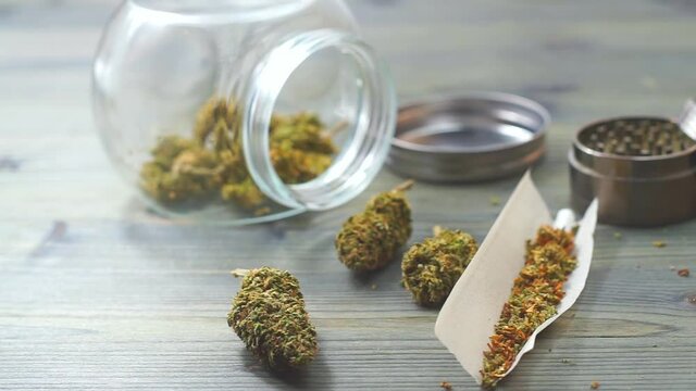 Close up of Marijuana joint essentials paper weed buds grinder and jar on wooden table