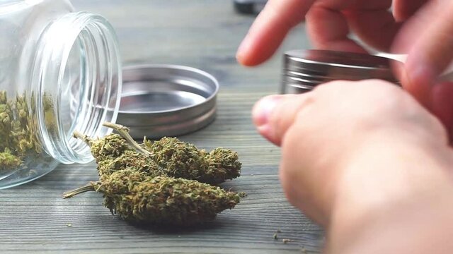 Close up of young man grinding Marijuana buds from jar on wooden table