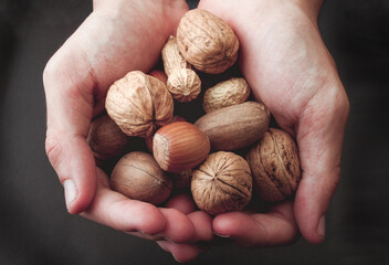 Various unpeeled nuts in hands on dark background