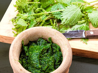cooked and raw nettles on a wooden board and in a rustic mortar